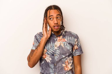 Genç Afrikalı Amerikalı adam beyaz arka planda izole edilmiş bir şekilde bir dedikoduyu dinlemeye çalışıyor..