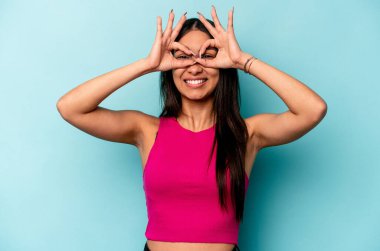 Mavi arka planda izole edilmiş genç İspanyol kadın gözlerinde sorun olmadığını gösteriyor.