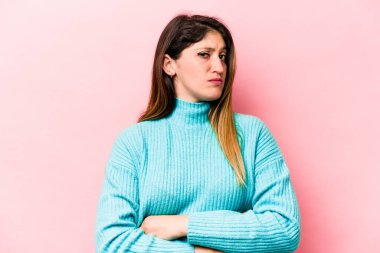 Pembe arka planda izole edilmiş genç beyaz kadın alaycı bir ifadeyle kameraya bakıyor..