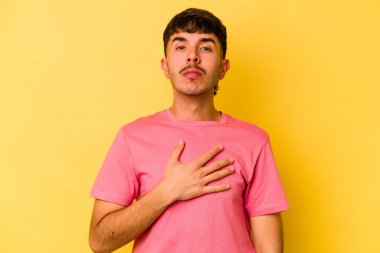 Sarı arka planda izole edilmiş genç beyaz adam yemin ediyor, elini göğsüne koyuyor..