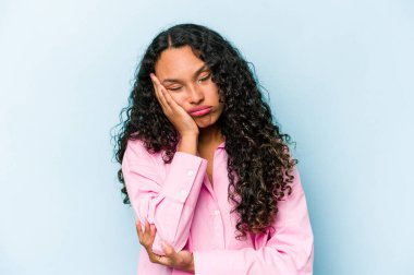 Mavi arka planda izole edilmiş genç İspanyol kadın. Sıkılmış, yorgun ve dinlenmeye ihtiyacı var..