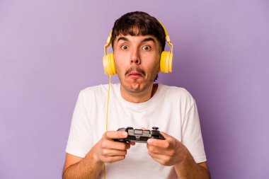 Mor arka planda izole edilmiş bir bilgisayar oyunu kontrolörüyle oynayan İspanyol genç adam omuzlarını silker ve gözleri açık kalır..