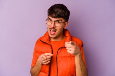 Mor arka planda izole edilmiş genç beyaz adam parmaklarıyla ön tarafı işaret ediyor..