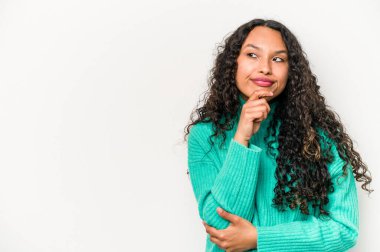 Beyaz arka planda izole edilmiş genç İspanyol kadın şüpheli ve şüpheci bir ifadeyle yana bakıyor..