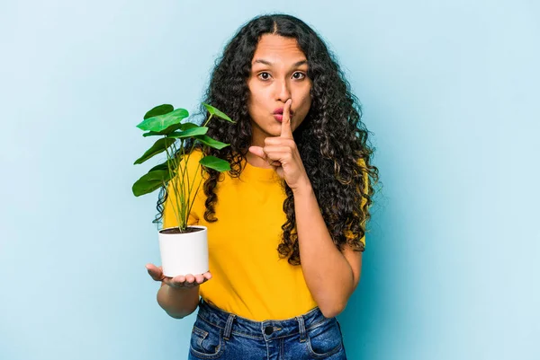 Jovem Hispânica Segurando Uma Planta Isolada Fundo Azul Mantendo Segredo — Fotografia de Stock