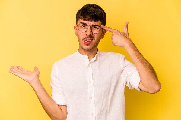 Young caucasian man isolated on yellow background holding and showing a product on hand.