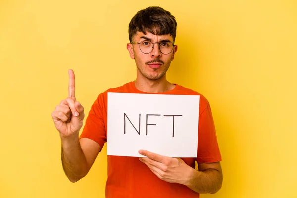 Mladý Hispánec Drží Nft Plakát Izolované Žlutém Pozadí Ukazující Číslo — Stock fotografie