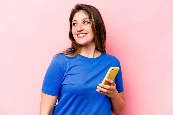 분홍색 배경에 고립된 전화를 코카서스 여성은 미소짓고 명랑하고 모습을 바라본다 — 스톡 사진