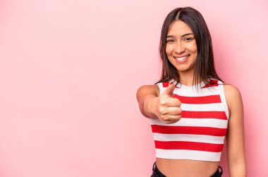 Genç İspanyol kadın pembe arka planda izole edilmiş gülümsüyor ve başparmağını kaldırıyor.