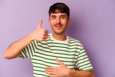 Mor arka planda izole edilmiş genç beyaz adam karnına dokunuyor, nazikçe gülümsüyor, yemek yiyor ve tatmin oluyor..