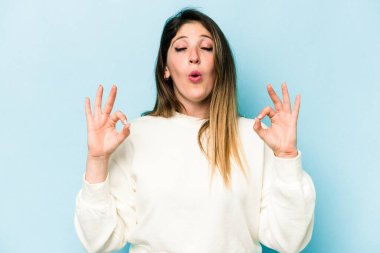 Mavi arka planda izole edilmiş genç beyaz kadın yoğun bir günün ardından rahatlıyor, yoga yapıyor..