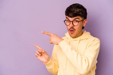 Mor arka planda izole edilmiş genç beyaz adam işaret parmağıyla fotokopi alanını işaret ederek heyecan ve arzusunu ifade ediyor..