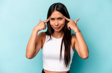 Mavi arka planda izole edilmiş genç İspanyol kadın bir işe odaklanmış, işaret parmaklarını işaret ediyor..