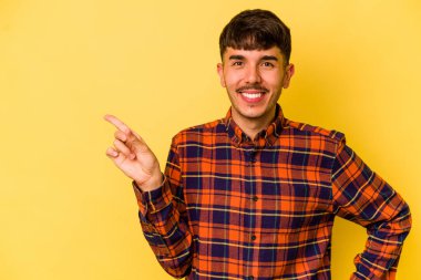 Sarı arka planda izole edilmiş genç beyaz adam işaret parmağıyla işaret ederek gülümsüyor..