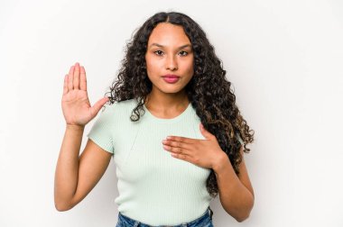 Young hispanic woman isolated on white background taking an oath, putting hand on chest.