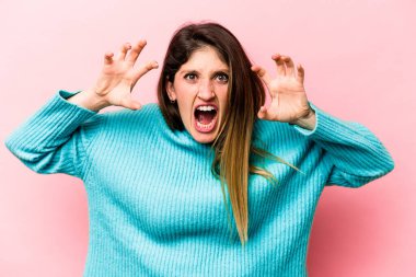 Pembe arka planda izole edilmiş genç beyaz kadın pençelerini kedi taklidi yaparken gösteriyor, agresif bir hareket..