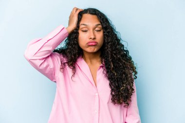 Mavi arka planda izole edilmiş genç İspanyol kadın yorgun ve uykulu ellerini başının üstünde tutuyor..