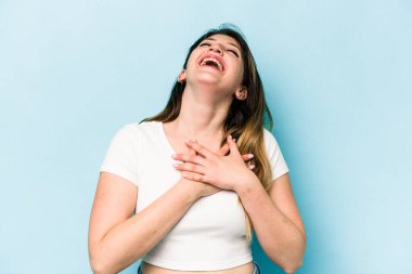Mavi arka planda soyutlanmış genç beyaz kadın gülüyor, elini yüreğine koyuyor, mutluluk kavramını koruyor..