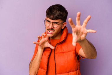 Mor arka planda izole edilmiş genç beyaz adam pençelerini kedi taklidi yaparken gösteriyor, agresif bir hareket..