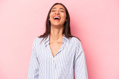 Genç İspanyol kadın pembe arka planda izole edilmiş rahat ve mutlu bir şekilde gülüyor, boynunda dişlerini gösteriyor..