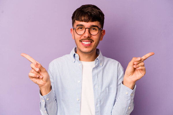 Young caucasian man isolated on purple background pointing to different copy spaces, choosing one of them, showing with finger.