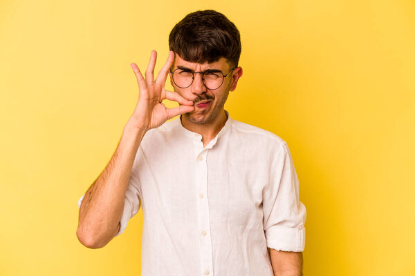 Young caucasian man isolated on yellow background with fingers on lips keeping a secret.