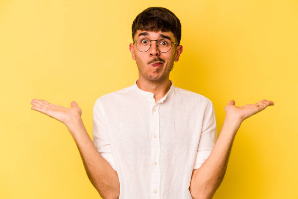 Young caucasian man isolated on yellow background confused and doubtful shrugging shoulders to hold a copy space.