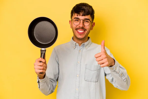 若いですヒスパニック炊飯器保持フライパン隔離された黄色の背景笑顔と親指アップ — ストック写真