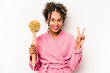 Sırt kaşıyıcısı tutan genç İspanyol kadın beyaz arka planda iki numarayı parmaklarıyla gösteriyor..