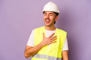 Mor arka planda izole edilmiş genç bir İspanyol işçi yüksek sesle gülüyor ve elini göğsüne koyuyor..