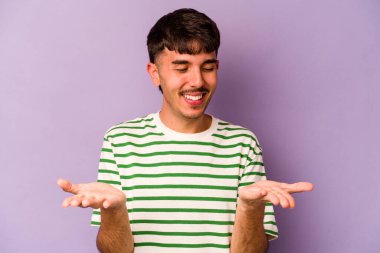 Mor arka planda izole edilmiş genç beyaz bir adam elinde avuç içi bir şeyle kameraya sunuyor..