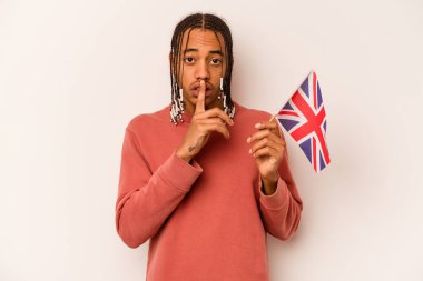 Beyaz arka planda izole edilmiş İngiliz bayrağı tutan genç Afrikalı Amerikalı bir adam ya sır saklıyor ya da sessizlik istiyor..