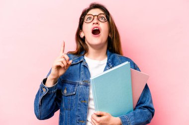 Pembe arka planda izole edilmiş genç beyaz kadın ağzı açık bir şekilde üst tarafı işaret ediyor..