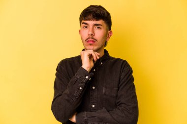 Genç beyaz adam sarı arka planda izole edilmiş şüpheli, belirsiz, seni muayene ediyor..