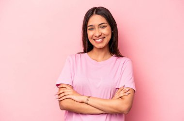 Pembe arka planda soyutlanmış genç İspanyol bir kadın. Kendinden emin, kararlılıkla kollarını kavuşturuyor..