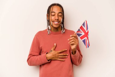 Beyaz arka planda izole edilmiş İngiliz bayrağı tutan genç Afrikalı Amerikalı adam elini göğsünde tutarak kahkahalar atıyor..