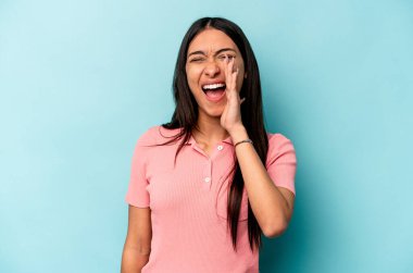 Genç İspanyol kadın mavi arka planda izole edilmiş, heyecanlı bir şekilde bağırıyor..