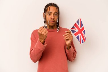 Beyaz arka planda izole edilmiş İngiliz bayrağı tutan genç Afrikalı Amerikalı adam yumruğunu kameraya gösteriyor, agresif yüz ifadesi..