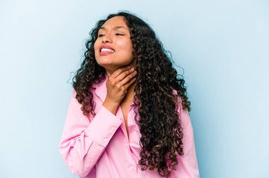 Mavi arka planda izole edilmiş genç İspanyol kadın virüs ya da enfeksiyon yüzünden boğaz ağrısı çekiyor..