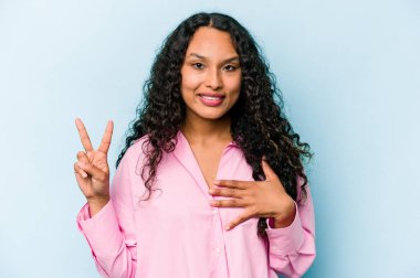 Genç İspanyol kadın mavi arka planda izole edilmiş yemin ediyor, elini göğsüne koyuyor..