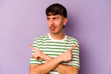 Mor arka plan noktalarında izole genç beyaz adam, iki seçenek arasında seçim yapmaya çalışıyor.