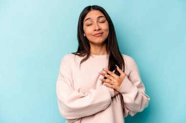 Mavi arka planda izole edilmiş genç İspanyol kadın avuçlarını göğsüne bastıran dostça bir ifadeye sahiptir. Aşk konsepti.