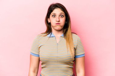 Pembe arka planda izole edilmiş genç beyaz kadın yanakları patlatıyor, yorgun bir ifade takınıyor. Yüz ifadesi kavramı.