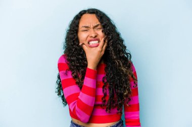 Mavi arka planda izole edilmiş genç İspanyol kadın güçlü bir diş ağrısı, azı dişi ağrısı var..