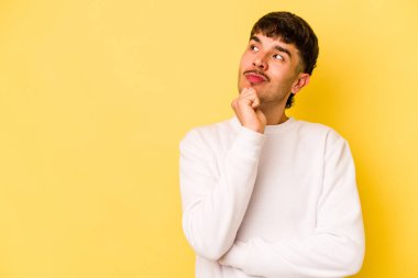 Sarı arka planda izole edilmiş genç beyaz adam şüpheli ve şüpheci bir ifadeyle yana bakıyor..