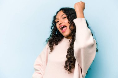 Mavi arka planda izole edilmiş genç İspanyol kadın zaferi, tutkuyu ve coşkuyu, mutlu ifadeyi kutluyor..