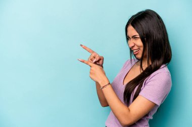 Genç İspanyol kadın mavi arka planda izole edilmiş başparmak uzakta, gülüyor ve kaygısız.