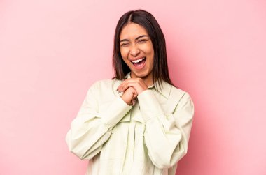 Pembe arka planda izole edilmiş genç İspanyol kadın ellerini çenesinin altında tutuyor ve mutlu bir şekilde yan tarafa bakıyor..