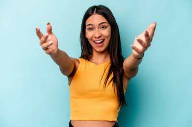 Genç İspanyol kadın mavi arka planda izole edilmiş zaferi ya da başarıyı kutluyor, şaşırmış ve şok olmuş..