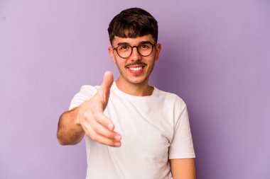 Mor arka planda izole edilmiş genç beyaz adam selamlama jesti olarak kameraya elini uzatıyor..